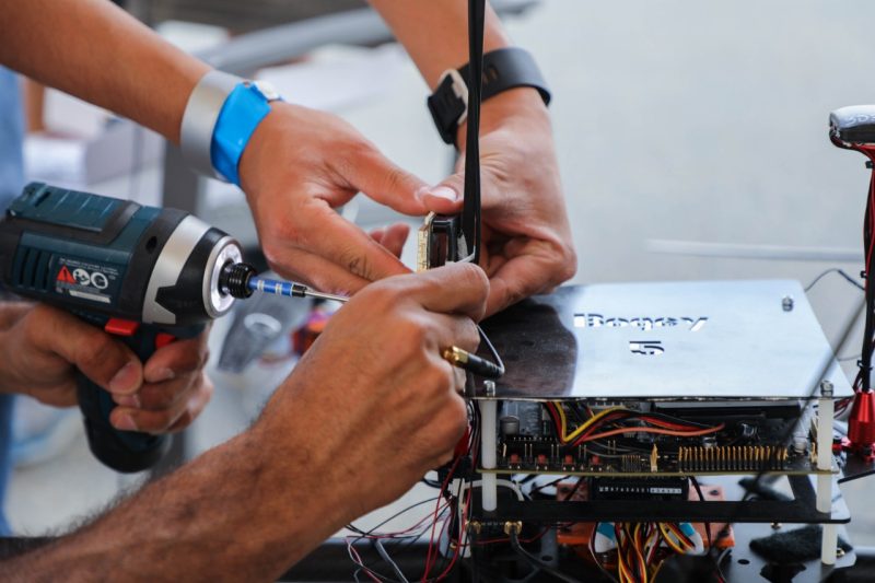 Close up of two pairs of hands working on a drone. One uses a drill.